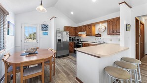 Una cocina moderna con armarios de madera, una isla central con taburetes, un refrigerador y una mesa de comedor con sillas.