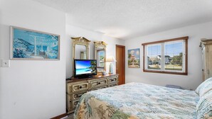 Un dormitorio con cama, cómoda, televisor y obras de arte.