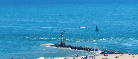 A beach with a rocky breakwater, umbrellas, and people sunbathing.