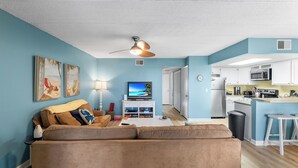 Ein Wohnzimmer mit braunem Sofa, einem Fernseher und einem Deckenventilator.