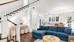 Un salón espacioso con un sofá seccional azul grande, una mesa de centro de madera y una escalera con barandillas blancas.