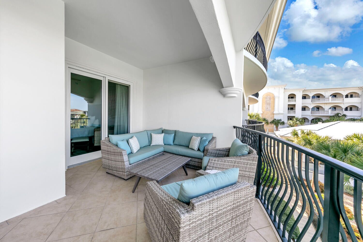 Un balcón con un sofá modular, un sillón de mimbre y vistas a un edificio con balcones.