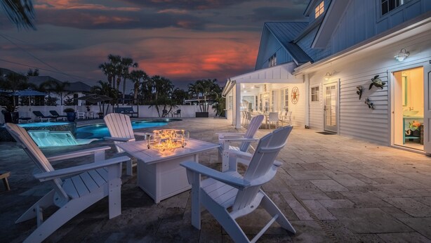 A pool area with lounge chairs and a fire feature, surrounded by a house with a porch and outdoor seating. - Steps to Vanderbilt Beach, Sleeps 13, Resort-Style Backyard (Naples)