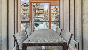 En inglasad uteplats med ett bord och stolar, utsikt över snötäckta byggnader och en klar himmel.