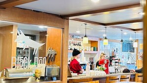 A restaurant interior with wooden furniture, a counter, and a person serving. - Mountain View Stoneridge - Pool & Hot Tub & Sauna (Canmore)