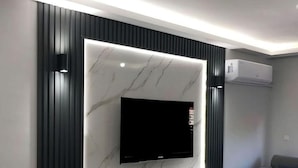 A modern living room with a flat-screen TV mounted on a marble wall, a built-in white entertainment unit below, and a grey sofa. - Setifana Sea view  (Conakry)