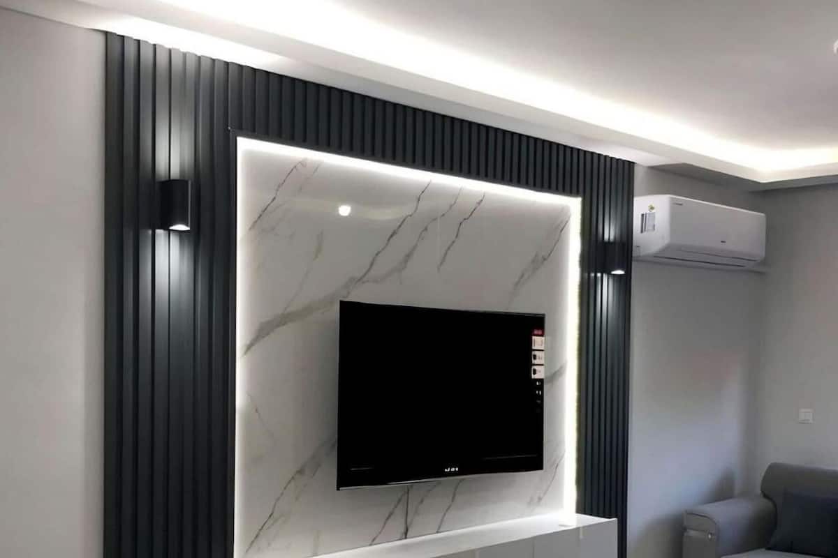 Ein modernes Wohnzimmer mit einem Flachbildfernseher an einer Marmorwand, darunter eine eingebaute weiße Unterhaltungseinheit und ein graues Sofa.