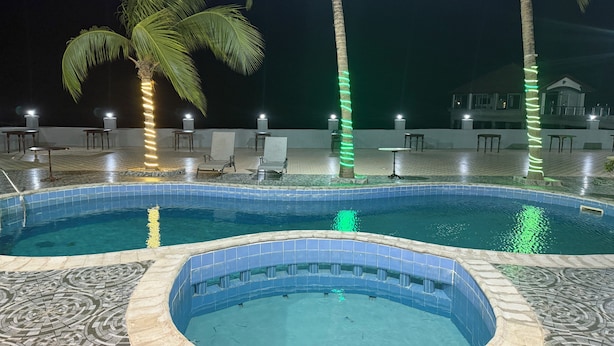 A swimming pool with tiled edges, surrounded by lounge chairs and palm trees. - Setifana Sea view  (Conakry)
