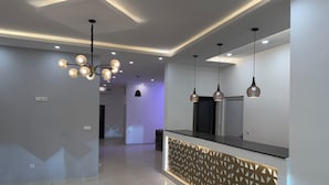 A modern hotel lobby with a geometric light fixture, a reception desk with a patterned partition, and pendant lighting. - Setifana Sea view  (Conakry)