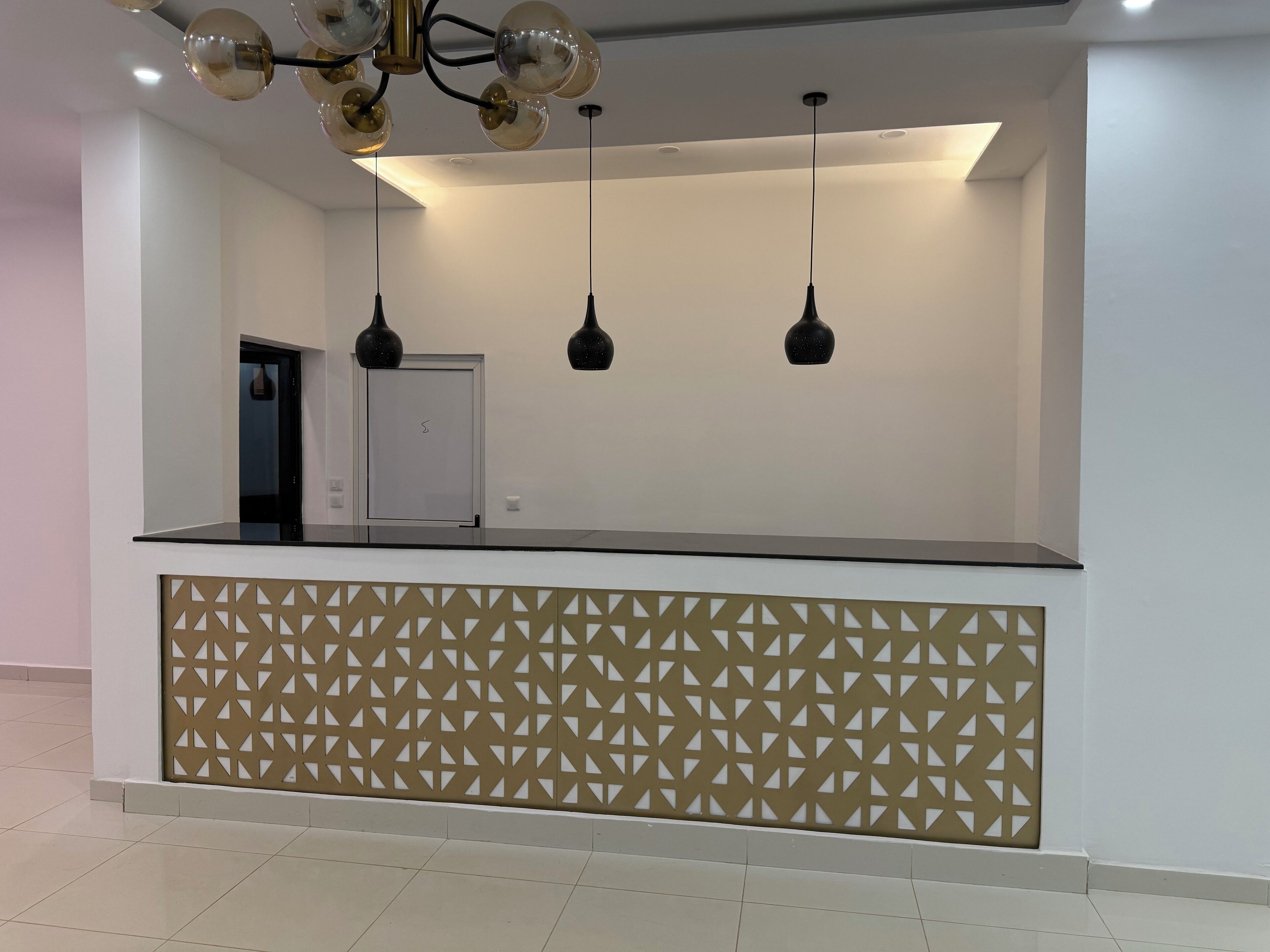 A reception area with a modern design, featuring a geometric patterned partition, a flat reception desk, and three pendant lights.