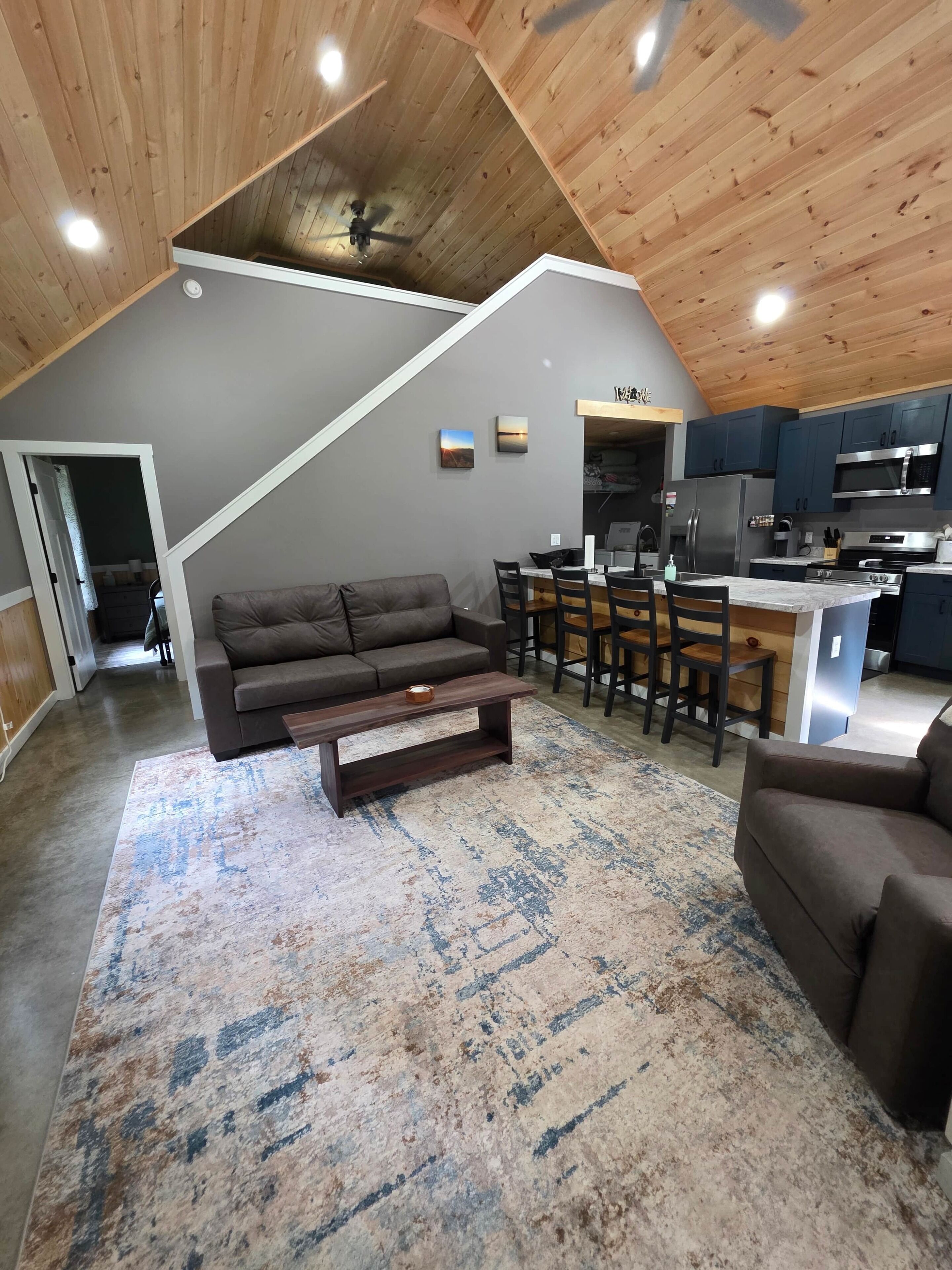 A spacious living area with a sofa, a coffee table, and a dining table with chairs. A kitchen area with modern appliances is visible in the background.