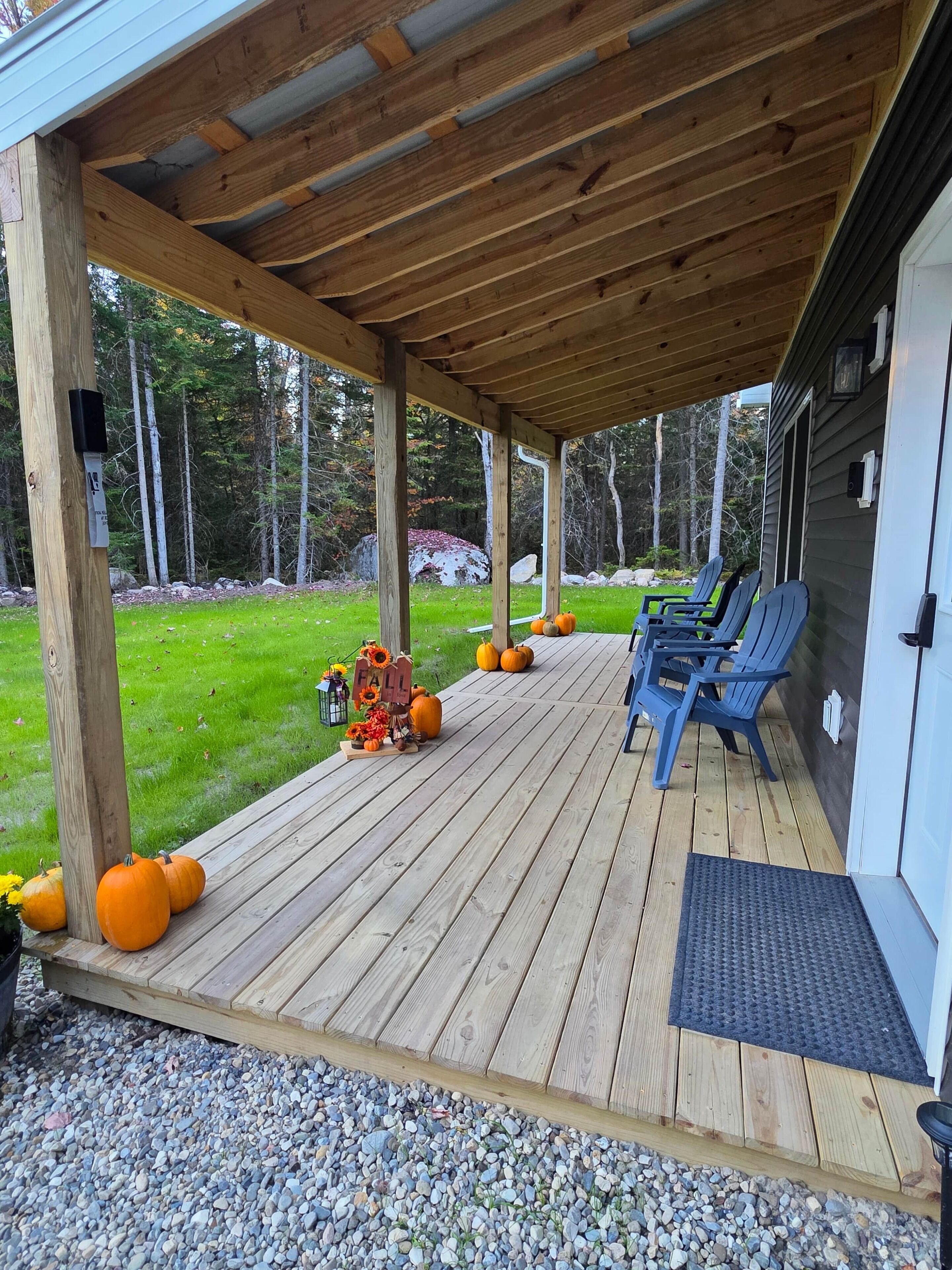 Un portico riparato con pavimento in legno, un tappetino d'ingresso e un'area relax con sedie.