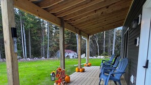A covered porch with wooden flooring, a doormat, and a seating area with chairs. - Adirondack Private & Cozy Cabin, close to ATV trails, Skiing, hiking and golfing (Owls Head)