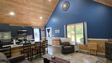 A spacious living area with a high ceiling, a kitchen with modern appliances, and a large window providing a view of the outdoors.