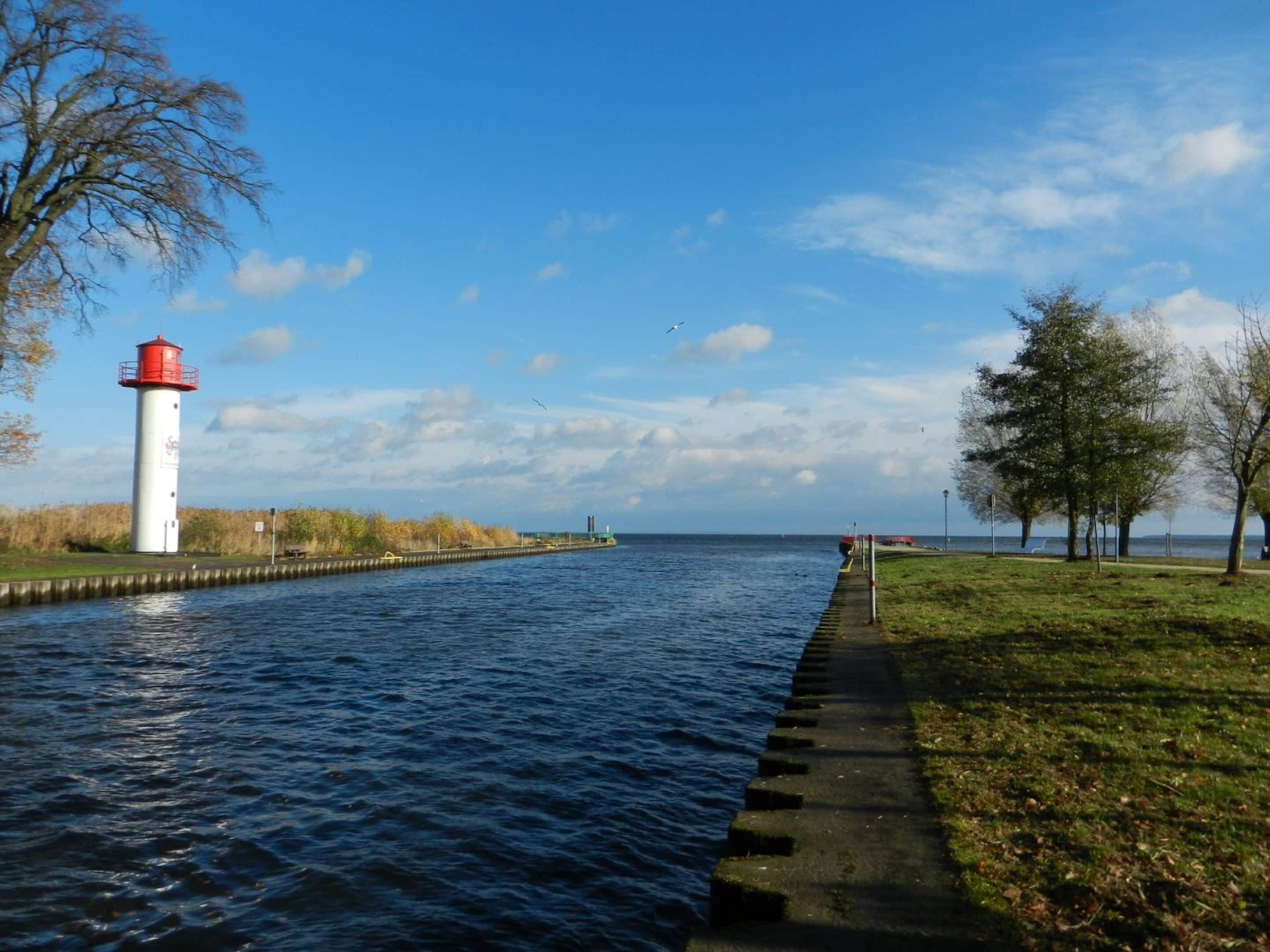 A lighthouse by a calm river with a grassy path and trees.