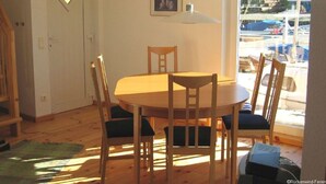 Un coin repas avec une table ronde et quatre chaises, une petite fenêtre donnant sur les voitures garées, et une porte avec un interrupteur.