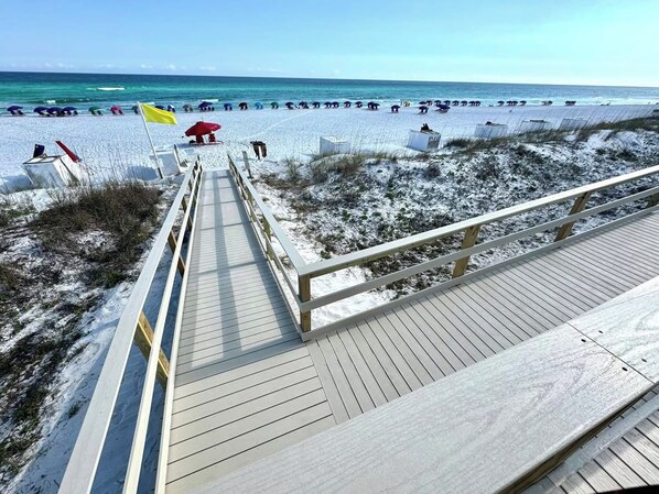 A wooden boardwalk leading to a beach with umbrellas and beach chairs.