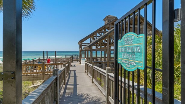 A wooden boardwalk leading to a beach pavilion entrance with a clear view of the ocean.