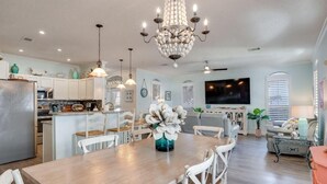 A spacious kitchen with white cabinets, a wooden dining table, and a chandelier.