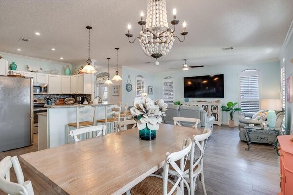 A spacious kitchen with white cabinets, a wooden dining table, and a chandelier.