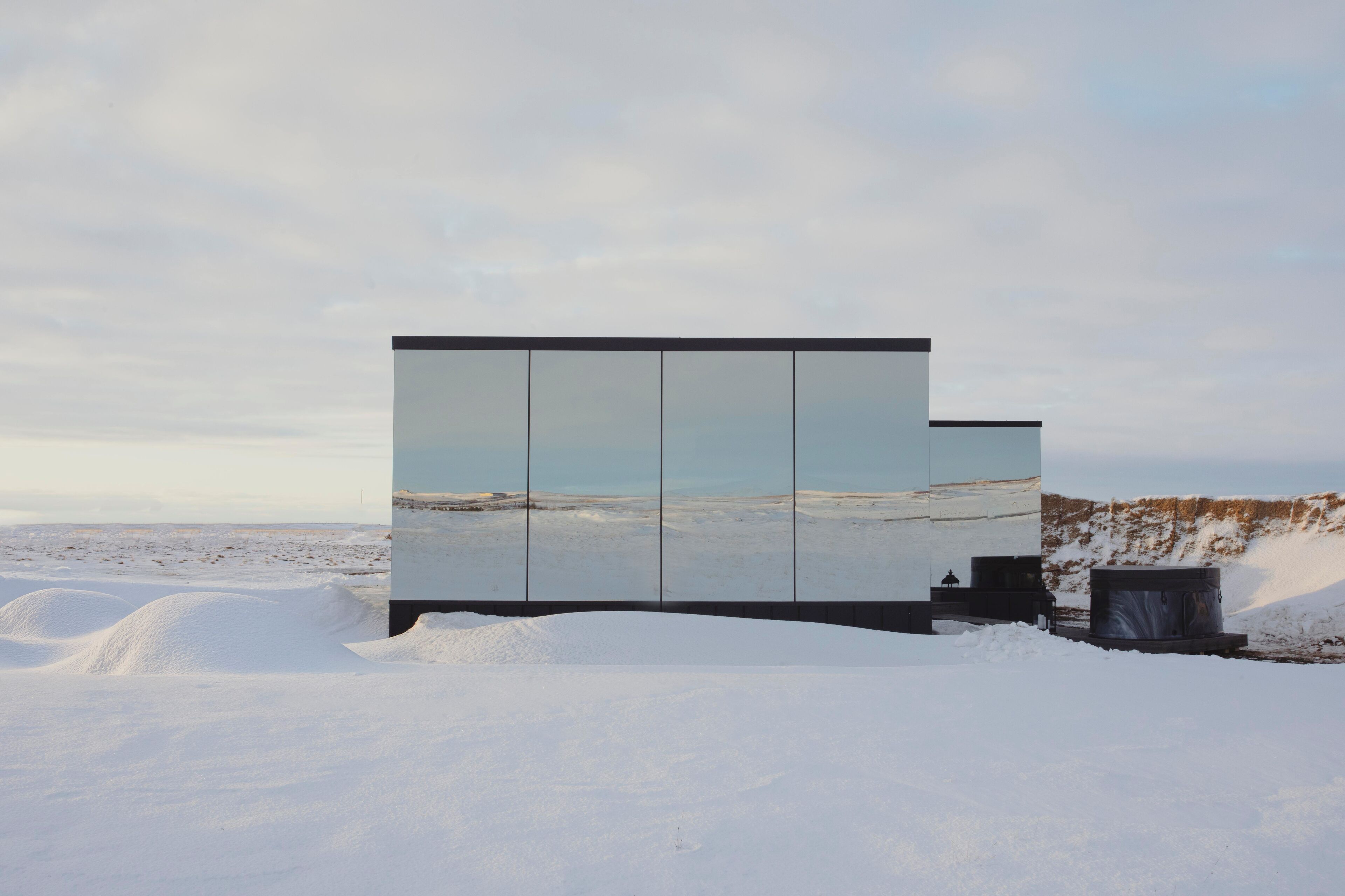 Un bâtiment moderne à la façade réfléchissante, situé dans un paysage enneigé.