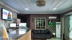 A reception area with a marble counter, two monitors, a black leather sofa, patterned wallpaper, and a chandelier. - Somewatt Fresh Hotel (Ilorin)