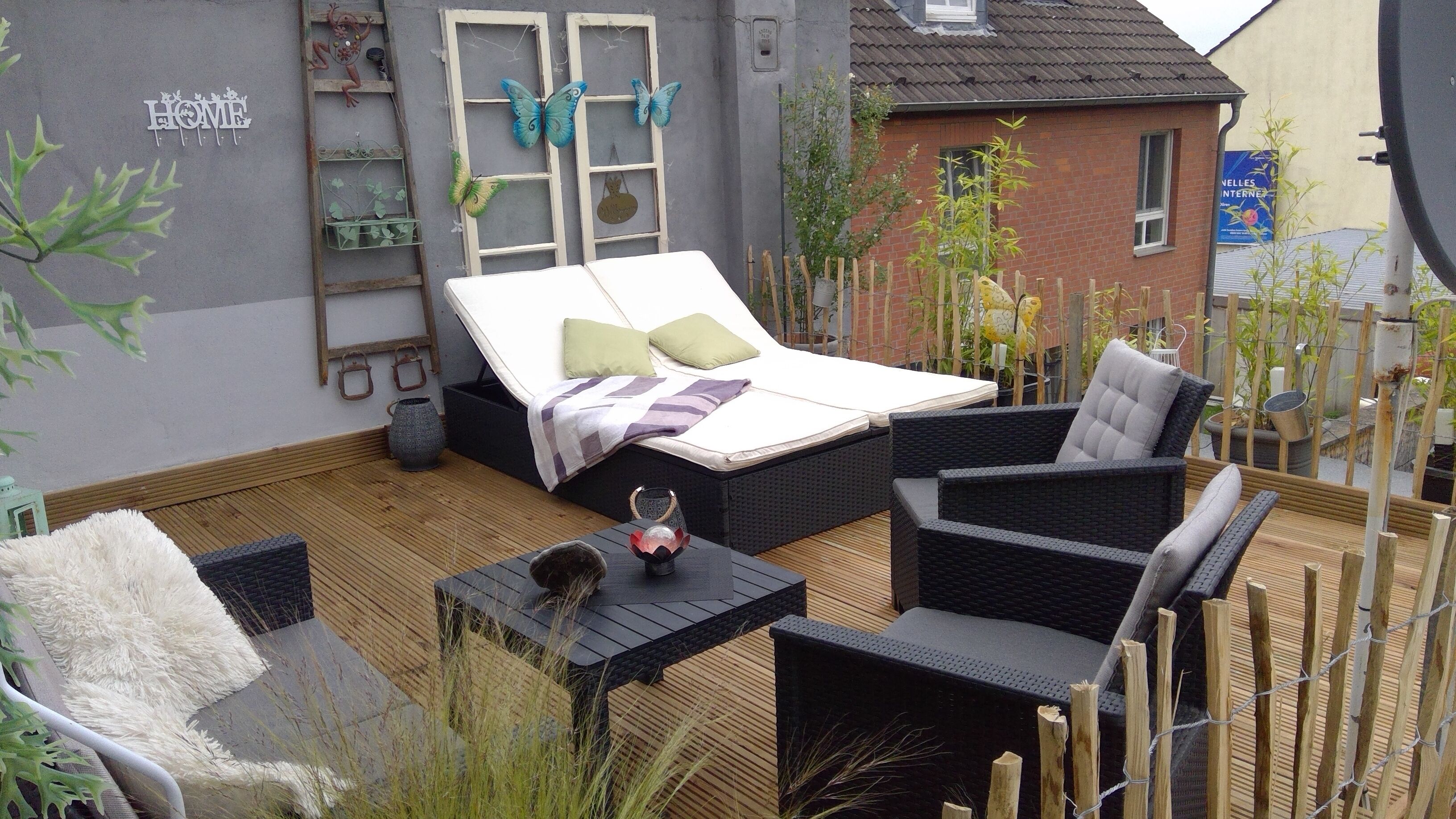 A sun loungers set up on a wooden deck with a small table and chairs, surrounded by decorative items and plants.