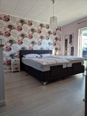 Ein Schlafzimmer mit einem großen Bett, einem Nachttisch, einer Kommode und einer Wand mit floralem Wandpapier.