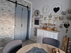 Ein Zimmer mit rustikaler Ziegelwand, einer blauen Schiebetür, einem weißen Schrank mit Dekoration und einem runden Holztisch mit Kissen.