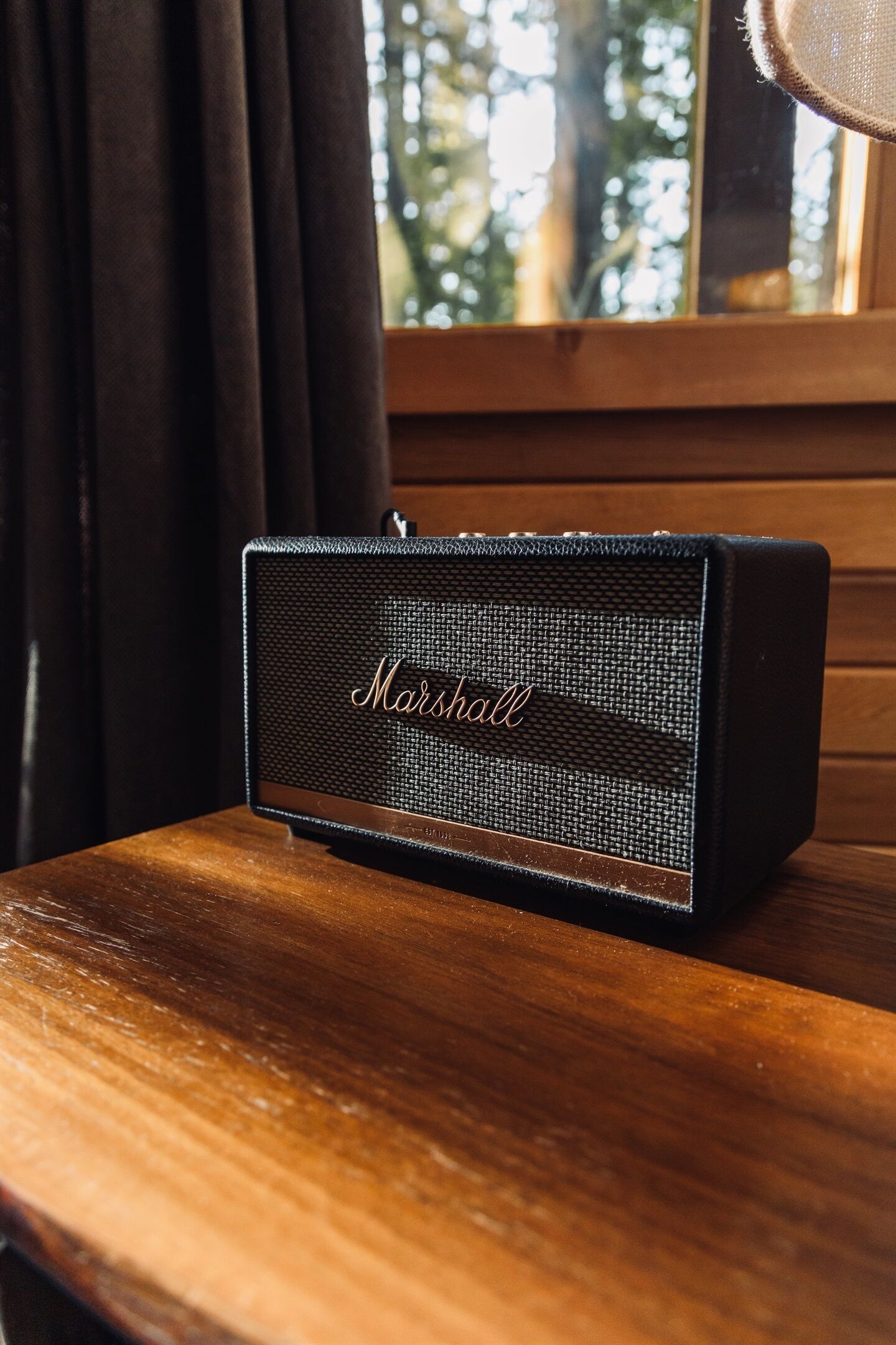 A Marshall speaker on a wooden surface near a window with curtains.