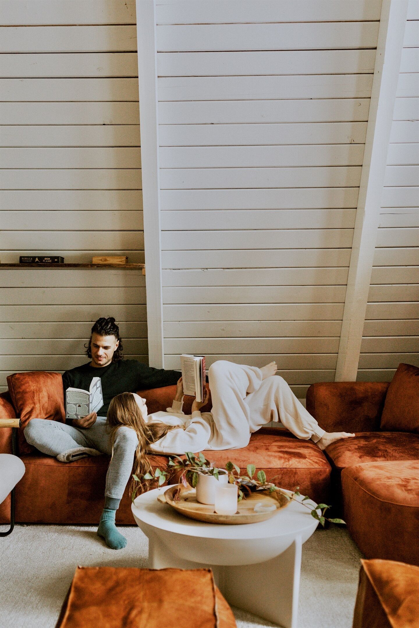 A cozy living room with a brown sofa, a white coffee table, and a bookshelf against a white paneled wall.