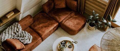 Un salon chaleureux de style loft, avec un canapé d’angle, une table basse et une grande fenêtre agrémentée de rideaux.