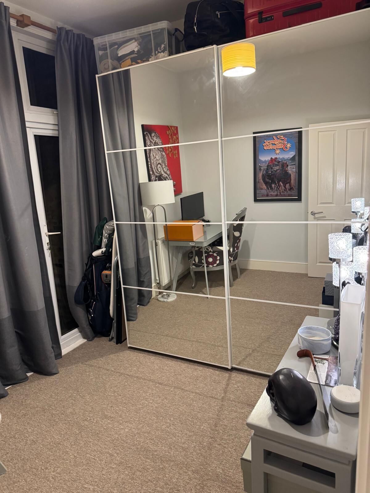 A room with a large mirror, a desk with a lamp, a chair, and a coat rack.