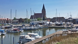 Un port de plaisance avec des bateaux amarrés, une église dotée d’un clocher imposant et des bâtiments en arrière-plan.