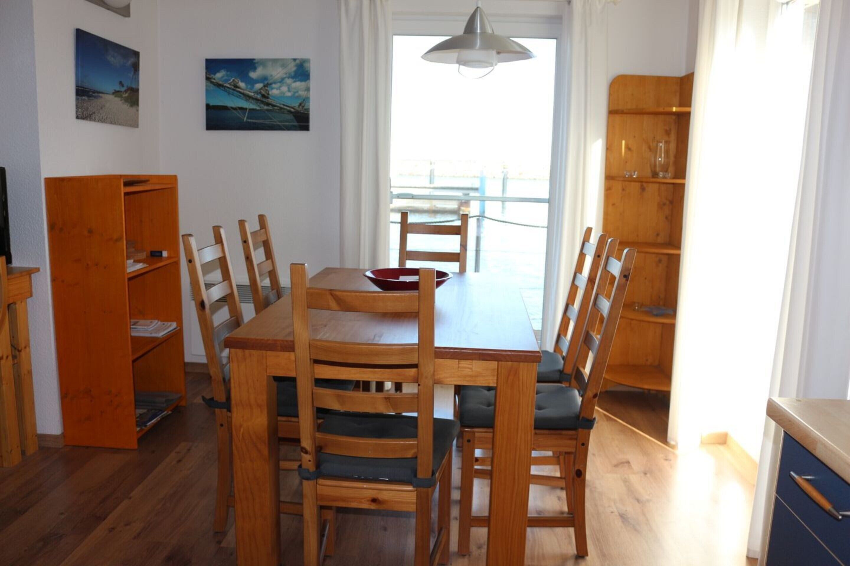 A dining area with a wooden table and chairs, a bookshelf, and a view through a window.