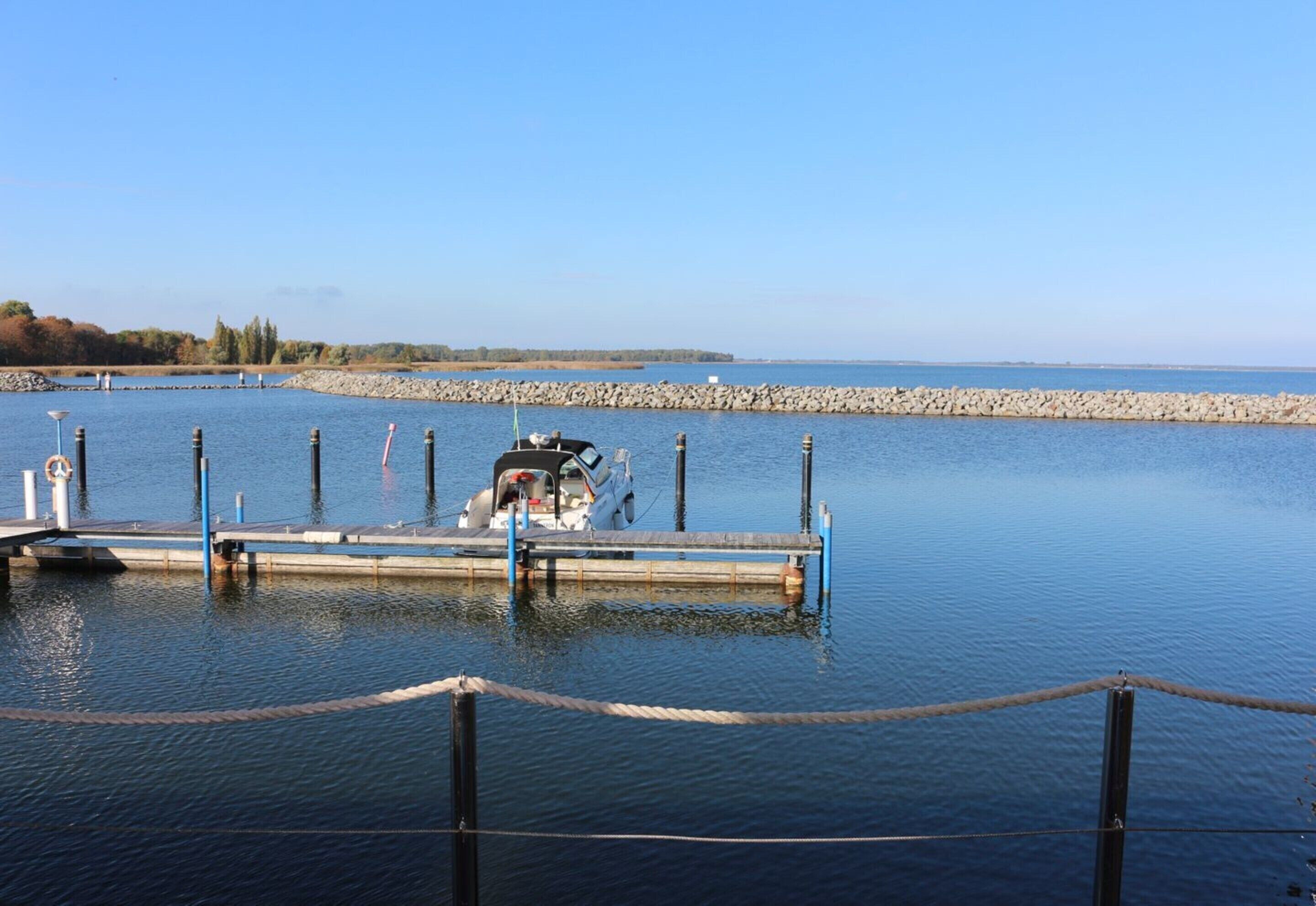 A dock with a boat moored at the end, surrounded by calm water and a clear sky.