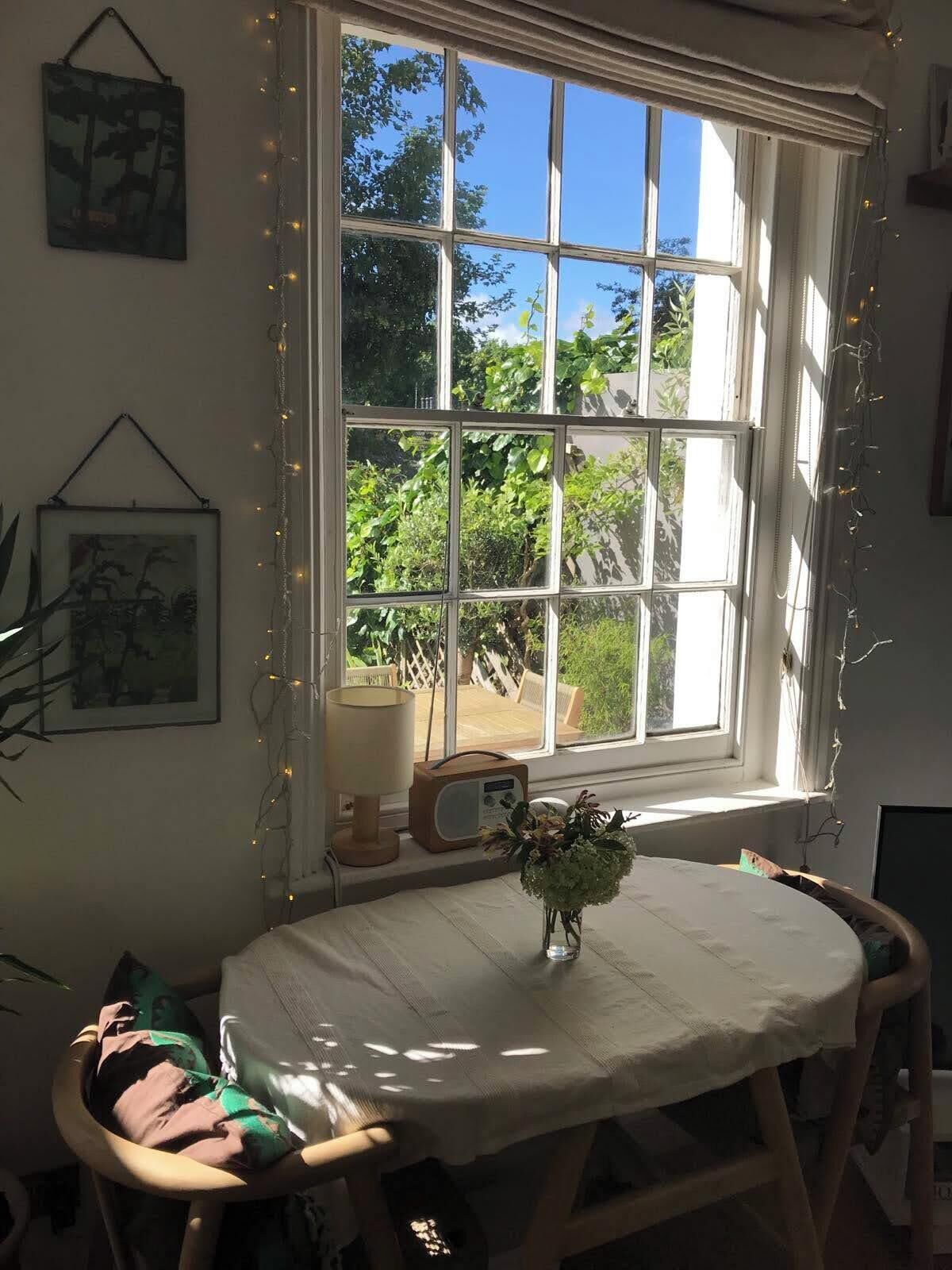 Ein Zimmer mit einem großen Fenster, einem Tisch mit Blumen in einer Vase und einem Stuhl.