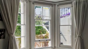 A room with three windows, each with curtains tied back, revealing a view of greenery and a building outside.