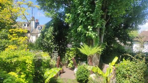 A lush garden with a variety of plants and trees, a pathway, and a view of a building in the background.