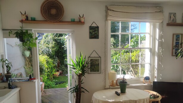 A room with a large window, a potted plant, a table with a white tablecloth, and a television on a stand.