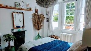A bedroom with a bed, a dresser, a mirror, a window with curtains, and a hanging light fixture.