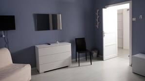 Un dormitori amb un aparador blanc, una cadira negra, una televisió i una porta que condueix a una altra habitació.