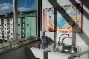 A kitchen with a window, a sink, and a painting of fruit.