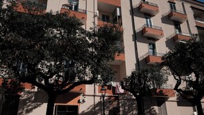 Un edifici d'altes plantes amb balcons, arbres al davant i cotxes aparcats.