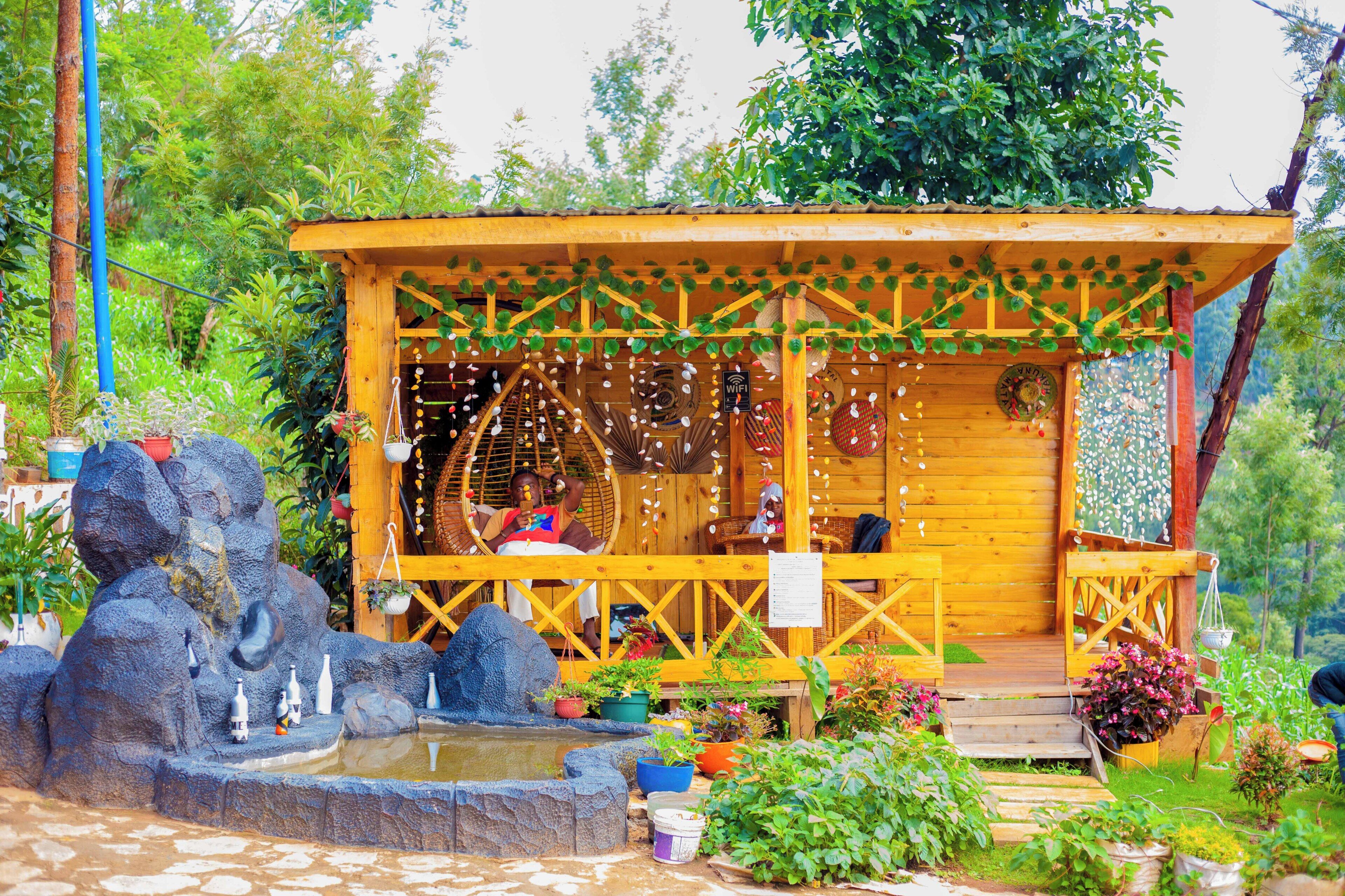 A wooden cabin with a porch, surrounded by greenery and a small pond.