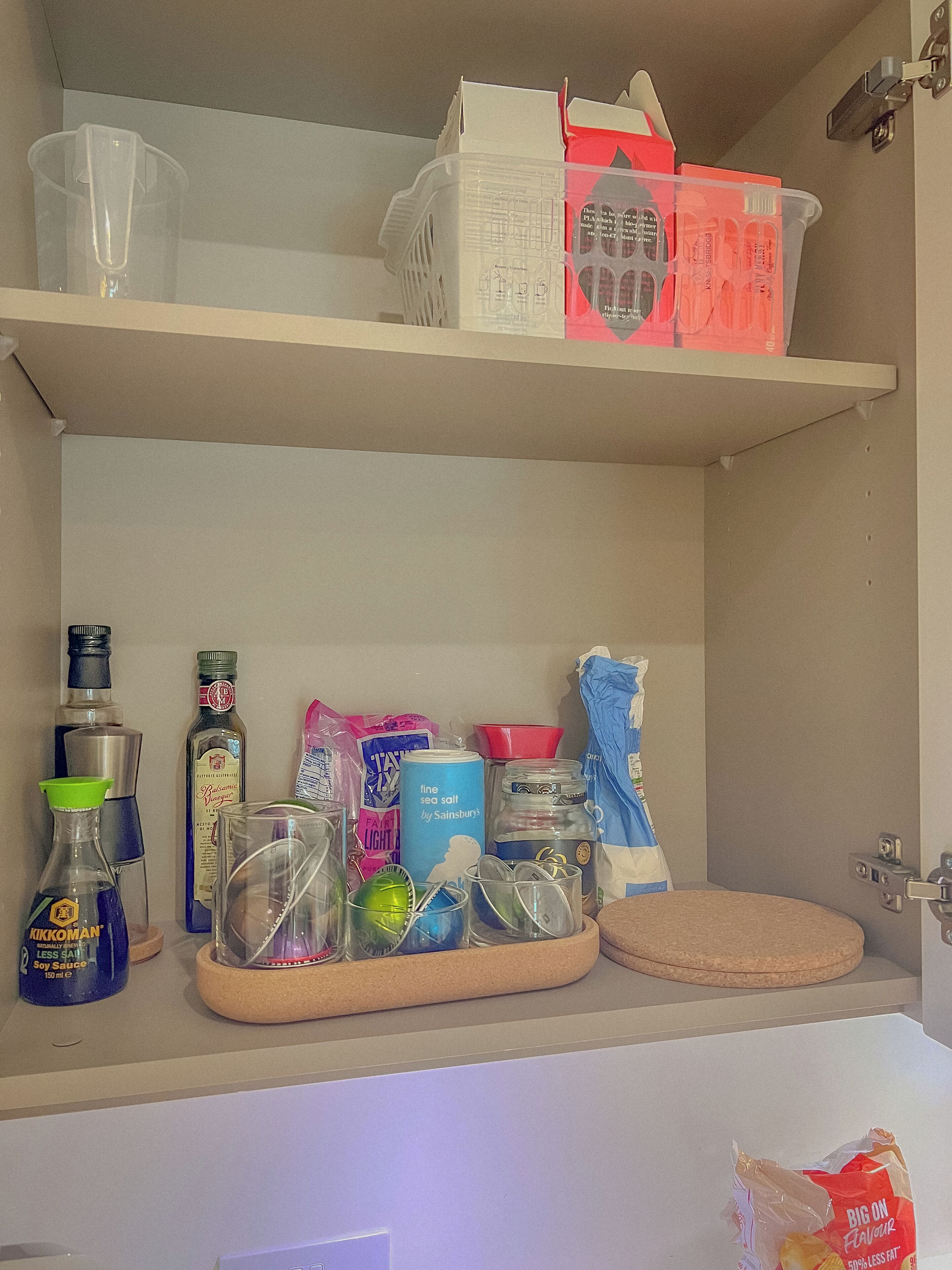 Een badkamer met een toilet, een wastafel en een plank boven de wastafel waarop verschillende voorwerpen staan, zoals een fles sojasaus, een pot zeezout en een plastic zak.