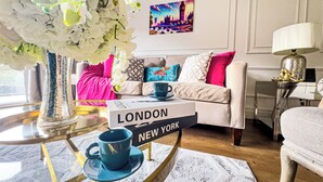 A living room with a white sofa, a coffee table with a blue mug, a vase with white flowers, and a painting of a cityscape on the wall.