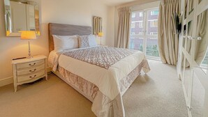 A hotel bedroom with a large bed, a nightstand, a mirror, and a window with curtains.