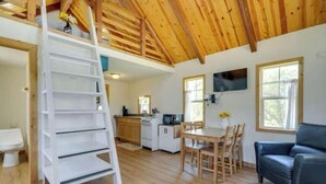 A wooden interior with a loft bed, a dining area, and a kitchen. - Lost Cabins #3 Kingsley's Kottage (Fredericksburg)