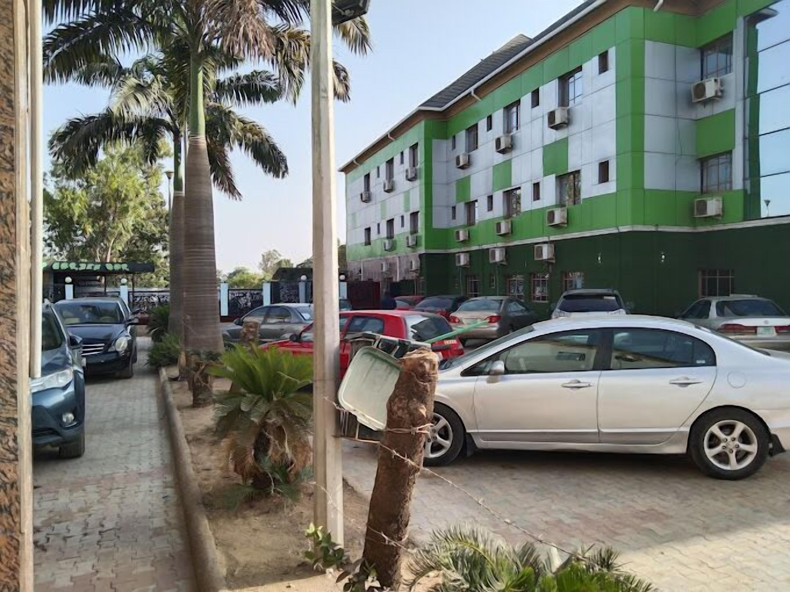 Un edificio de varios pisos con paredes exteriores verdes y blancas, coches aparcados y palmeras.